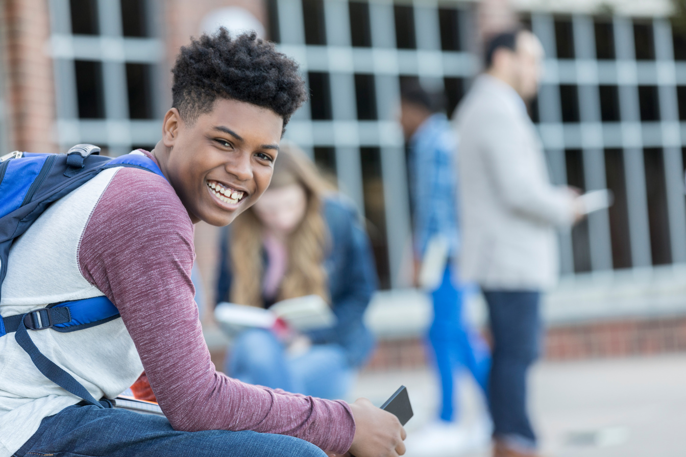 Happy African American teen boy sitting outside high school